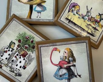 Könnte beinhalten: Vier quadratische Untersetzer mit Holzrahmen, die Illustrationen aus Alice im Wunderland zeigen. Einer zeigt eine Raupe auf einem Pilz, einer eine Teeparty, einer Spielkartenfiguren beim Rosenbemalen und einer ein Mädchen mit einem Flamingo.
