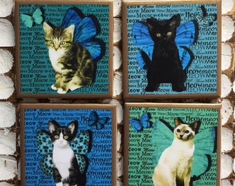Puede incluir: Cuatro posavasos cuadrados de cerámica con fondo azul y verde. Cada posavasos presenta un gato diferente con alas de mariposa. El texto "Meow" se repite en cada posavasos.