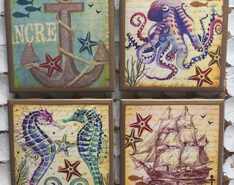 May include: Set of four square ceramic tiles with a nautical theme. Each tile features a different image: an anchor with rope, an octopus, two seahorses, and a sailing ship. The tiles have a distressed, vintage look with a gold border.