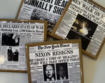 Op de afbeelding: Vier vierkante onderzetters met historische krantenvoorpagina's: The Dallas Times Herald over de dood van JFK, The New York Times over de maanlanding, The Charleston Daily Mail over de oorlog in Hawaï en The New York Times over het aftreden van Nixon.