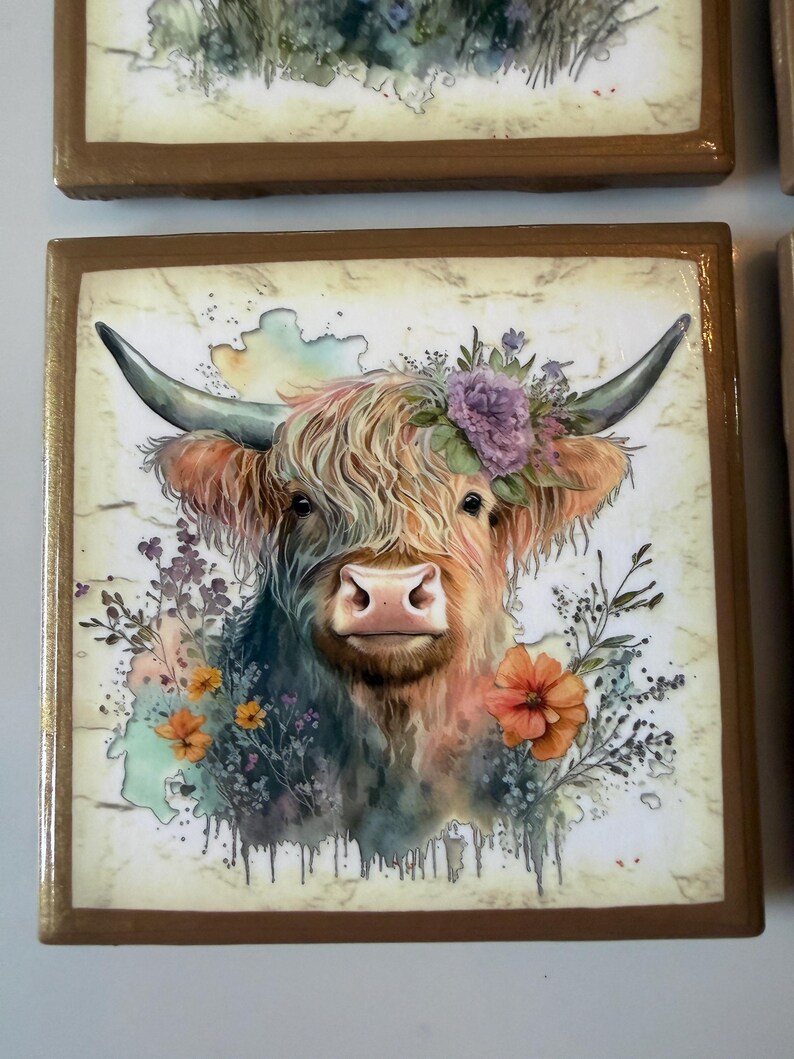 Puede incluir: Un azulejo decorativo cuadrado con una ilustraci&oacute;n estilo acuarela de una vaca Highland con pelaje largo y desgre&ntilde;ado, cuernos curvados y una corona de flores moradas y naranjas. El fondo tiene una textura color crema tipo m&aacute;rmol con gotas.