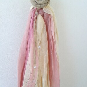May include: A white candle with a pink and cream fabric decoration. The fabric is tied with a brown ribbon and has a small pearl embellishment.