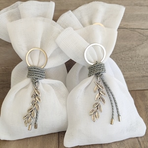 May include: Two white fabric pouches with silver keychains and olive branch charms. The pouches are tied with gray rope and have a delicate, sheer texture.