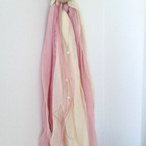 May include: A white candle with a pink and cream fabric tassel and a beige fabric flower with a pearl accent.