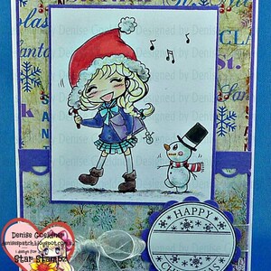 May include: A Christmas card featuring a cartoon girl wearing a red Santa hat and a blue coat, singing with a microphone. A snowman with a black top hat and red scarf stands next to her. The card has a purple border and a blue background with snowflakes. The text "Happy Christmas" is written in a circle on the bottom right corner of the card.
