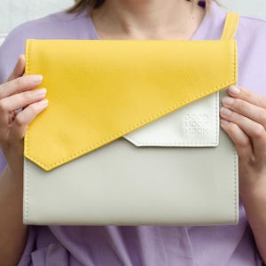 May include: A yellow and white leather clutch with a flap closure. The clutch has a white patch with the text "GOOD MOOD NOW" on it.