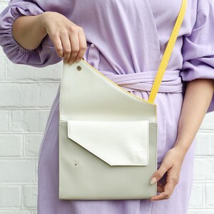 May include: A light purple dress with a yellow strap and a white and gray crossbody bag.