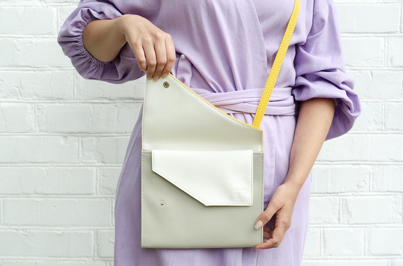May include: A light purple dress with a yellow strap and a white and gray crossbody bag.