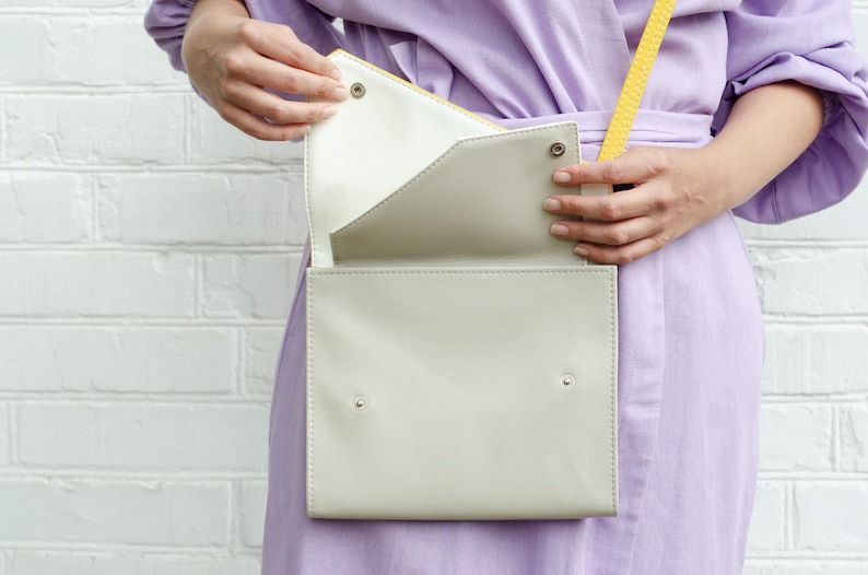 May include: A light gray leather crossbody bag with a yellow strap. The bag is open and the inside is white.