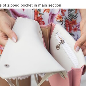 May include: A white and pink handbag with a zippered pocket. The pocket is open and the zipper pull is visible. The bag has a gold chain strap.