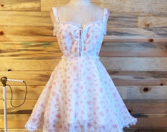 May include: A white dress with a pink floral pattern and lace trim. The dress has a sweetheart neckline and thin straps.