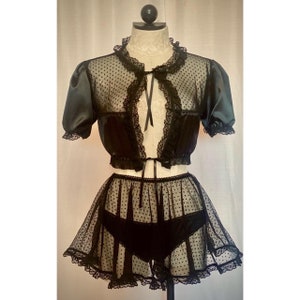 Könnte beinhalten: Schwarzes, durchsichtiges Dessous-Set mit Tupfenmuster. Das Oberteil ist ein verkürzter Bolero mit Spitzenbesatz und einem Band am Hals. Der Rock ist ein Minirock mit Spitzenbesatz und einem schwarzen Satinbund.