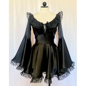 Puede incluir: Un vestido de satén negro con una superposición de encaje y mangas acampanadas. El vestido tiene un escote de corazón y un corpiño ajustado. La falda es amplia y fluida.