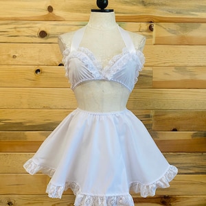 Op de afbeelding: Witte lingerie set met kant, bestaande uit een haltertop en een kort rokje. De top heeft een satijnen lint om te strikken en het rokje heeft een gerimpelde kanten rand.
