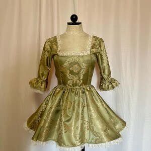 Peut inclure: Une robe en brocart vert et or avec un décolleté carré et des bordures en dentelle. La robe a un corsage ajusté et une jupe ample.
