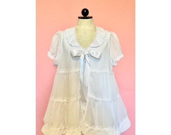 May include: A white dress with a ruffled neckline and a white satin ribbon tied at the waist. The dress has a tiered skirt with lace trim.