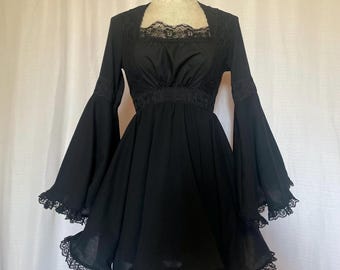 Pode incluir: Um vestido preto curto com mangas compridas bufantes e acabamento em renda. O vestido tem um decote quadrado e um corpete justo.