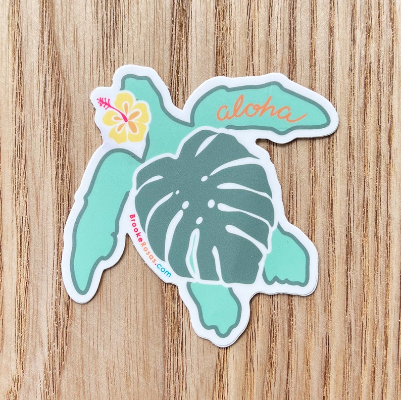 Puede incluir: Una pegatina de tortuga azul turquesa con una hoja de monstera verde, una flor de hibisco amarilla y la palabra "Aloha" en escritura naranja.
