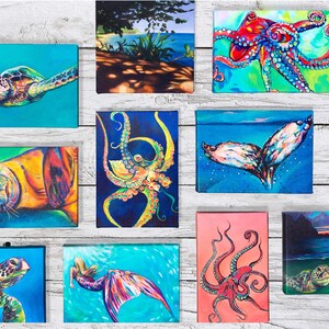 May include: A collection of 10 colorful paintings featuring various sea creatures, including a turtle, octopus, whale tail, seal, and mermaid. The paintings are displayed on a white wooden background.
