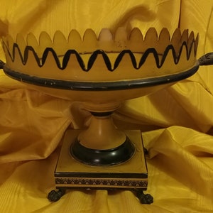 May include: A gold and black decorative bowl with a scalloped rim and a pedestal base. The bowl has a black and gold trim around the rim and base.