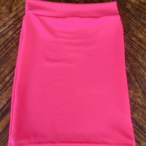 May include: A bright pink mini skirt made of a textured fabric. The skirt has a simple design and a straight cut.