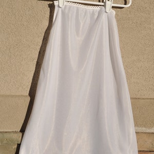 May include: White slip with a lace trim. The slip is made of a silky material and is hanging on a white hanger.
