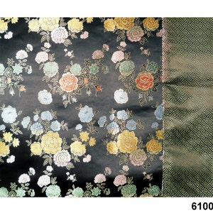 May include: Black fabric with a floral pattern in shades of pink, yellow, blue, and green. The fabric has a subtle sheen and a textured surface. The fabric is paired with a solid green fabric with a geometric pattern.