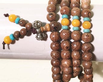 May include: A brown wooden beaded bracelet with yellow and blue beads. The bracelet has a metal charm with a decorative design.