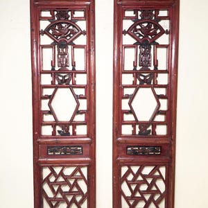 May include: A pair of antique Chinese red wood lattice panels with intricate carvings. The panels feature a geometric design with a hexagonal center and a decorative motif at the top.
