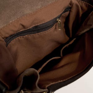 May include: Open view of a black leather bag's interior, revealing a brown fabric lining and multiple pockets. A black zipper runs across the top, and a gold-colored zipper pull is visible. The bag's interior is well-lit, showcasing the details.