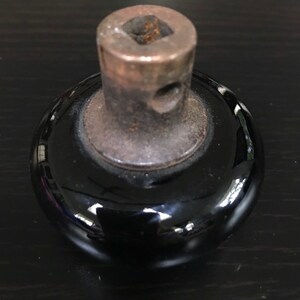 May include: Black ceramic knob with a metal base and a square hole in the top. The knob is smooth and shiny.