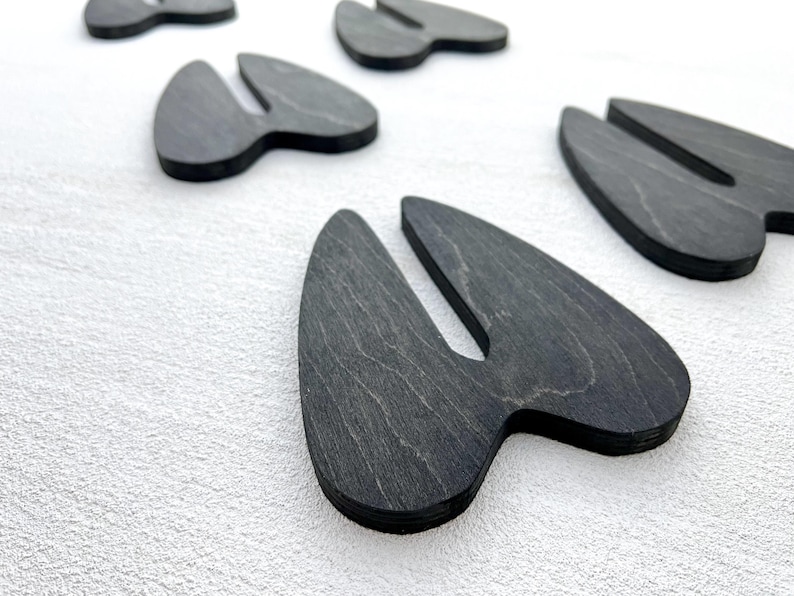 K&ouml;nnte beinhalten: F&uuml;nf schwarze Schiefer-Untersetzer in Form eines Hirschabfruchs. Die Untersetzer sind versetzt auf einer wei&szlig;en Oberfl&auml;che angeordnet.