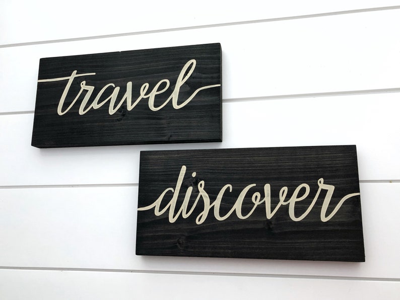 May include: Two wooden signs with the words "travel" and "discover" written in white cursive script on a black background.