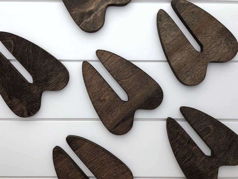 K&ouml;nnte beinhalten: Sechs dunkelbraune, aus Holz ausgeschnittene Formen, die an Hirschschenkel erinnern. Die Formen sind in einem Muster auf einer wei&szlig;en Oberfl&auml;che angeordnet.