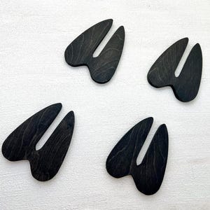 K&ouml;nnte beinhalten: Vier schwarze, tierische Hufformen aus Holz, m&ouml;glicherweise Hirschufe, auf wei&szlig;em Hintergrund.