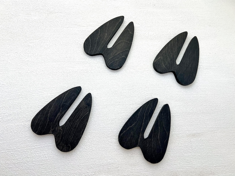 K&ouml;nnte beinhalten: Vier schwarze, tierische Hufformen aus Holz, m&ouml;glicherweise Hirschufe, auf wei&szlig;em Hintergrund.