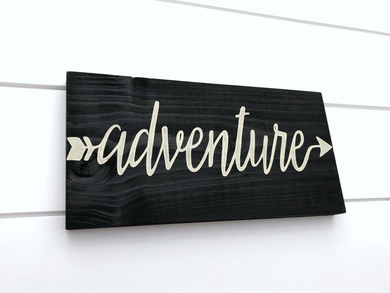 May include: Black wooden sign with the word "adventure" written in white script with an arrow pointing to the right.