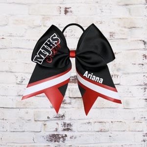 May include: Black cheer bow with white and red stripes. The bow has the text "MHS Cheer" and the name "Ariana" on it.