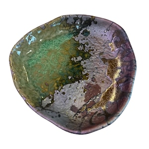 May include: A small, irregularly shaped ceramic dish with a green, purple, and gold glaze. The dish has a textured surface and a slightly raised rim.