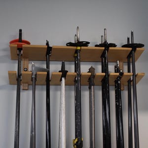 May include: A wooden wall-mounted rack with multiple ski poles hanging from it. The poles are black and white and have different types of tips.
