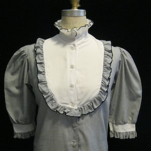May include: A white and black striped button-up shirt with a white ruffled collar and cuffs. The shirt has a white panel in the front with a ruffled trim.