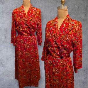 May include: A red vintage dress with a floral pattern. The dress features a wrap-style front with a V-neckline and long sleeves. The floral design includes shades of yellow, brown, and blue. The dress is displayed on a mannequin.