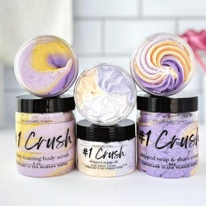 Könnte beinhalten: Eine Auswahl an Körperpflegeprodukten in transparenten Gläsern mit schwarzen Deckeln. Die Gläser sind mit "#1 Crush" beschriftet und enthalten geschlagene Seifen, Peelings und Körperbutter. Die Produkte haben einen Wirbel aus lila, gelben und weißen Farben. Der Text "eScentually Yours" ist sichtbar.