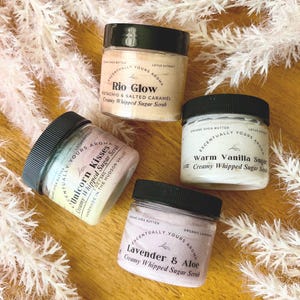 May include: Four glass jars of creamy whipped sugar scrub with different scents. The jars are labeled "Rio Glow", "Unicorn Kisses", "Warm Vanilla Sugar", and "Lavender & Aloe".