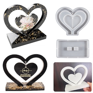 Pode incluir: Um molde de silicone de duas peças para fazer ornamentos de resina em forma de coração. O molde é feito de silicone transparente e tem um design em forma de coração com um coração menor dentro. O molde é mostrado com um ornamento de resina acabado em preto e dourado, e um ornamento de resina branco.