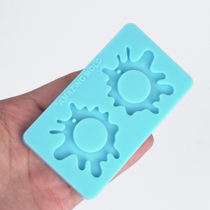 May include: A light blue silicone mold with two circular impressions surrounded by splash-like designs. The text "AMAZING MOLD" is printed on the mold. The mold is rectangular and held in a hand.