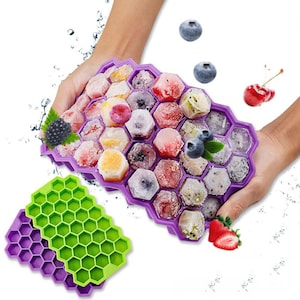 Puede incluir: Bandejas de cubitos de hielo de silicona de color morado y verde con un diseño de panal. Las bandejas están llenas de fruta y bayas congeladas.