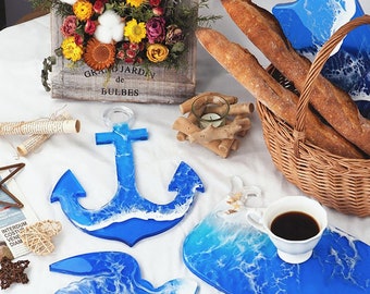 May include: Three resin serving trays in the shape of an anchor, a rectangle, and a freeform shape. The trays are blue and white with a wave design. The trays are on a white surface with a basket of bread, a flower arrangement, and a cup of coffee.