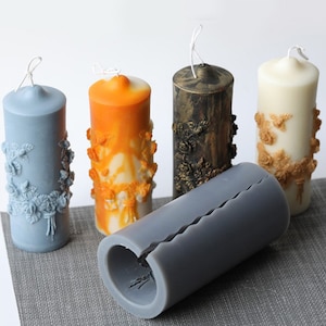 May include: Four decorative pillar candles with floral designs in blue, orange, gold, and brown. A gray silicone mold for making candles is also shown.