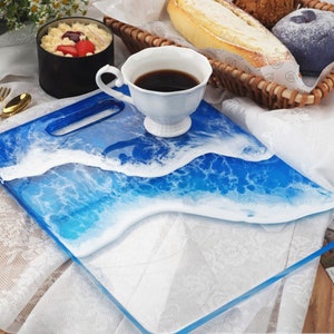 May include: A blue and white resin serving tray with a wave design. The tray has a handle and is perfect for serving snacks or drinks.
